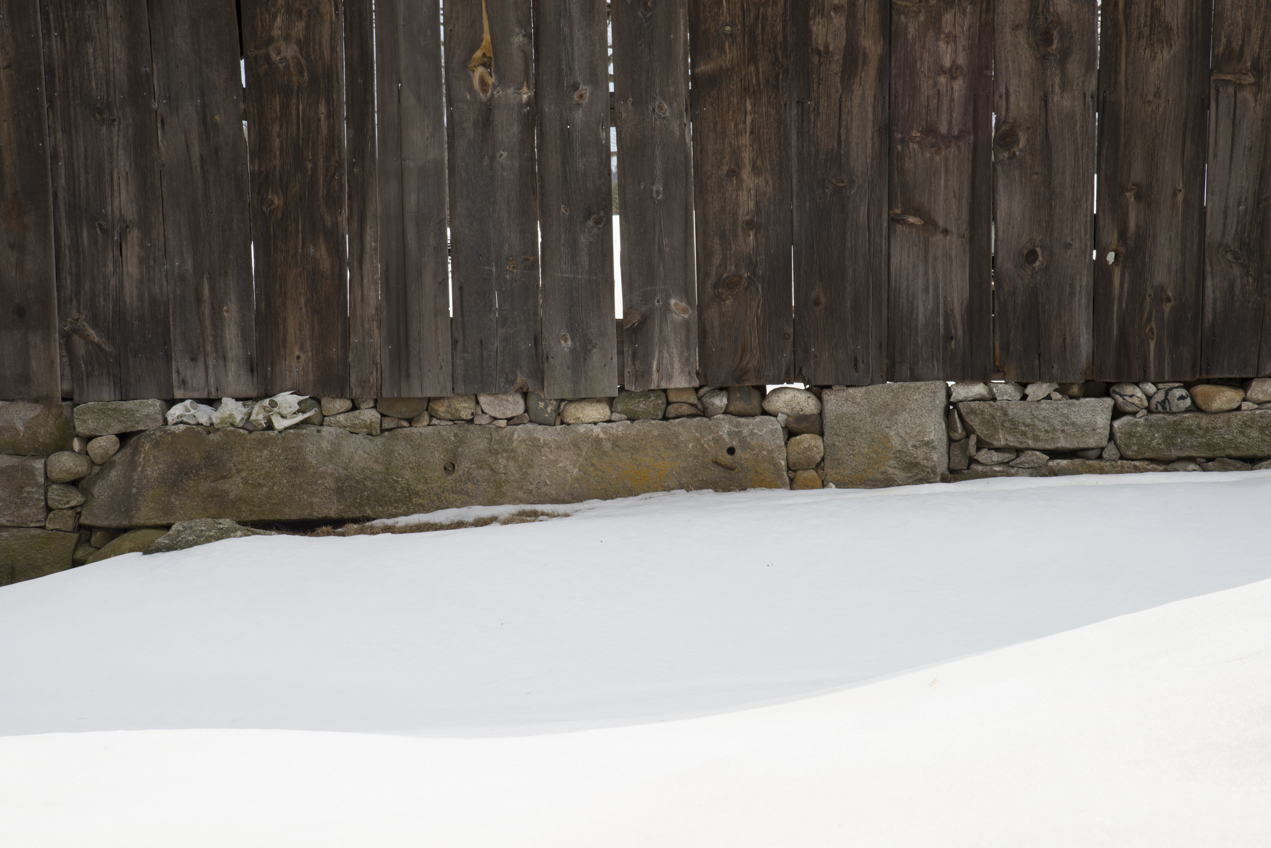 Weathered barn board and a stone foundation in fresh snow at the Shaker village.