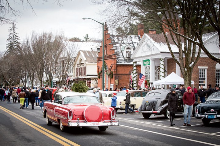 Tony Carlotto’s cherry-red vintage Mercury pulls onto Main Street with a small Christmas tree strapped to its roof—the centerpiece of the reenacted painting.