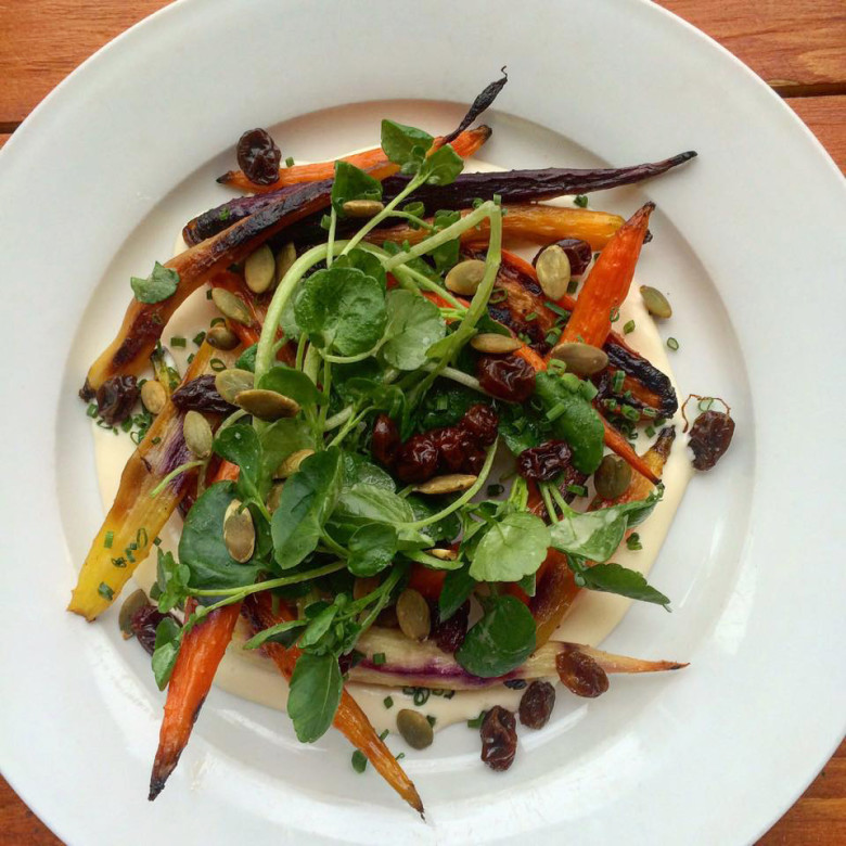 A salad of warm roasted carrots, pickled raisins, watercress, pepitas, and buttermilk dressing.