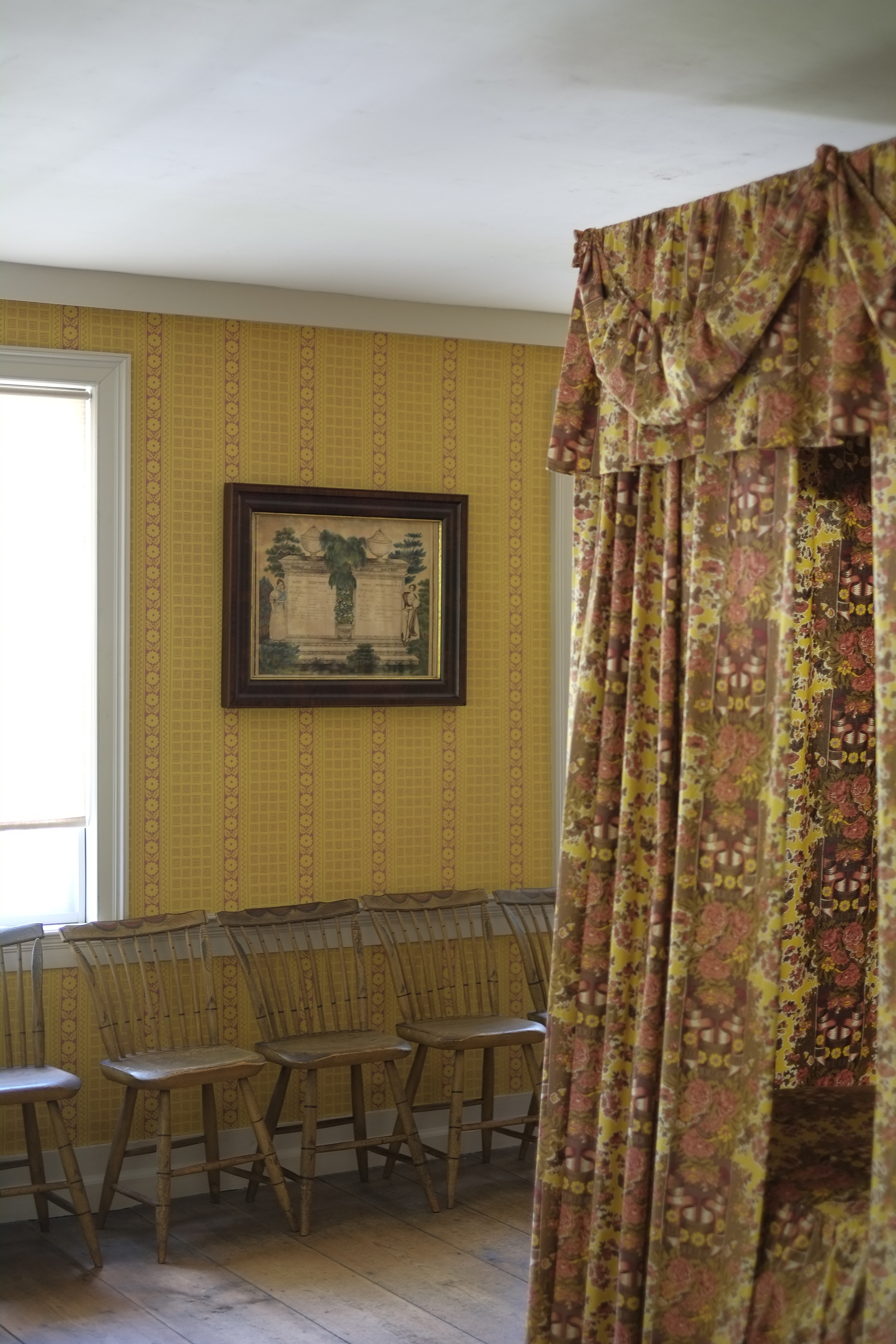 Yellow wallpaper, a canopied bed and a row of windsor chairs line a wall in an upstairs bedroom at Williams House.
